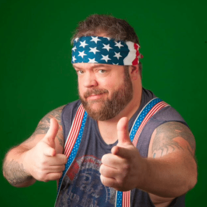 Bearded man wearing a star-spangled headband and American flag suspenders gives two thumbs up against a green background.