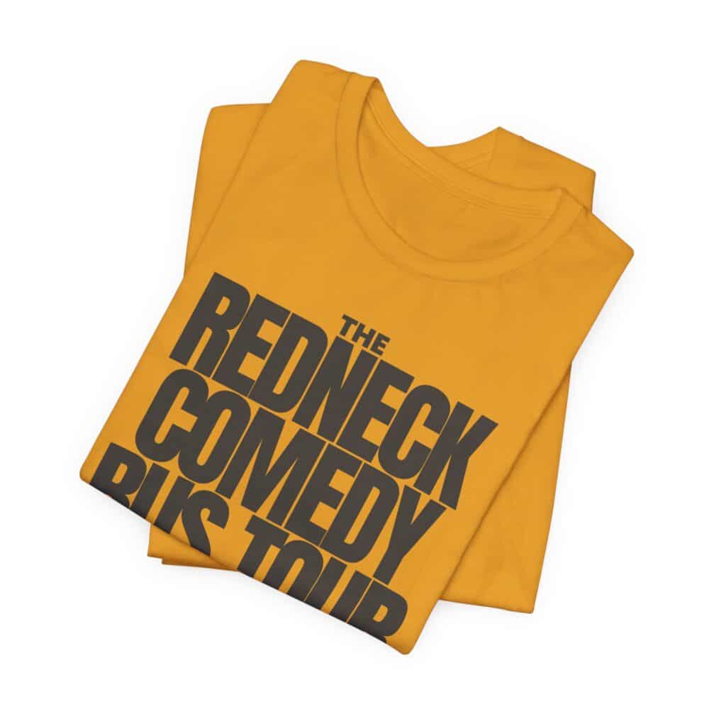 A folded yellow Redneck Comedy Bus Tour Tshirt with large black text on the front.