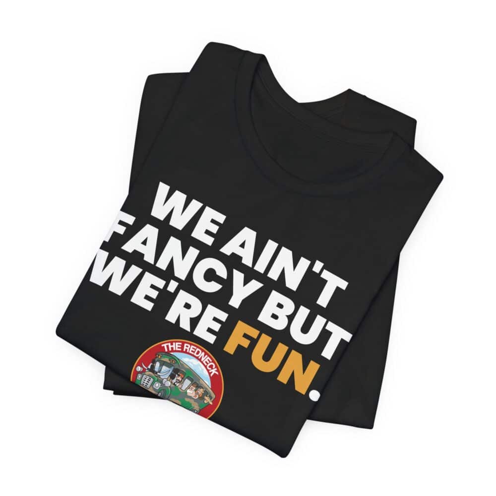 The We Ain't Fancy Tshirt is a folded black tee featuring "WE AIN'T FANCY BUT WE'RE FUN." in bold white and yellow letters, plus a small colorful graphic in the lower corner.