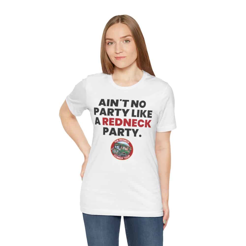 A woman poses with one hand on her hip, wearing the "Ain't No Party - Redneck Tshirt," a white shirt featuring the phrase "AIN'T NO PARTY LIKE A REDNECK PARTY" and a round graphic underneath.