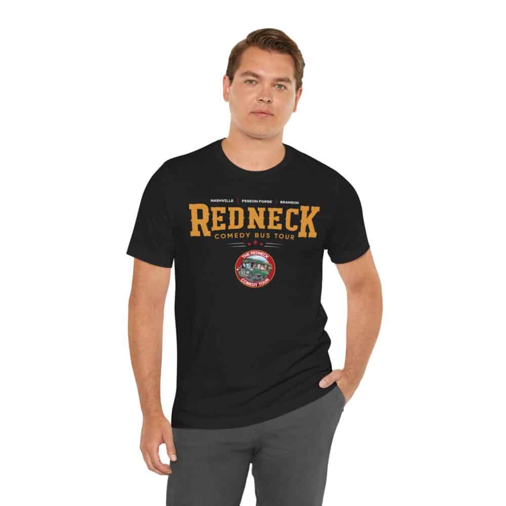 Man wearing the Redneck Comedy Bus Tour Tshirt featuring "Redneck Comedy Bus Tour" text and a small circular logo at the center, standing with one hand in his pocket.