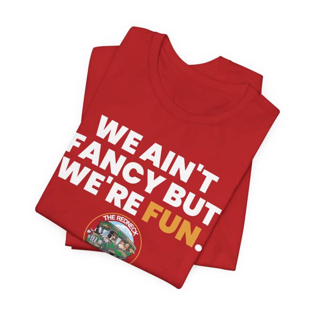 A folded We Ain't Fancy Tshirt in red features “WE AIN'T FANCY BUT WE'RE FUN.” printed on it with a small cartoon logo that says "THE REDNECK.