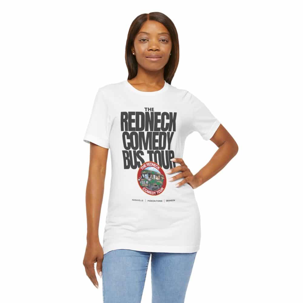 A woman poses with one hand on her hip, wearing the Redneck Comedy Bus Tour Tshirt, a white top featuring "The Redneck Comedy Bus Tour" text and a circular graphic underneath.