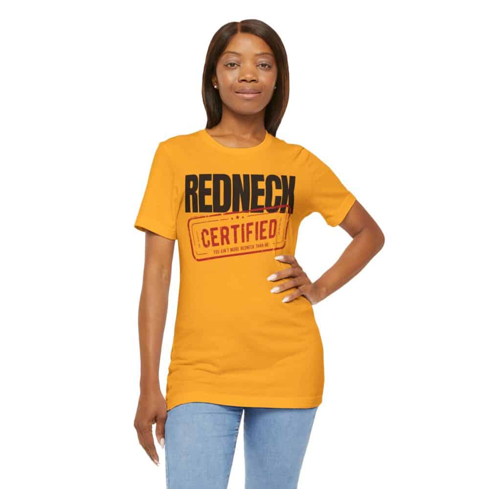 A woman stands facing forward against a white background, one hand on her hip, wearing the Redneck Certified Tshirt in yellow and light blue jeans.