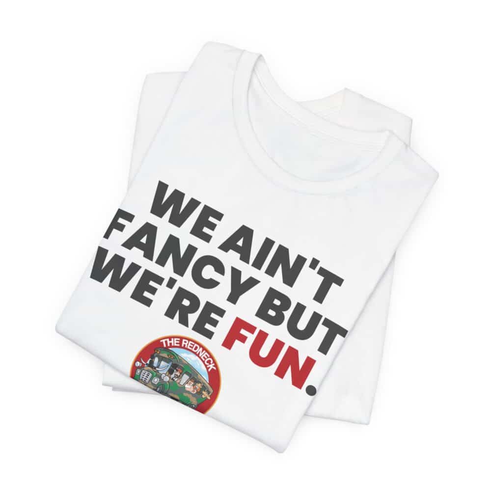 The We Ain't Fancy Tshirt is a white tee, neatly folded, featuring "WE AIN'T FANCY BUT WE'RE FUN." in bold black and red letters with a small colorful circular graphic near the bottom.