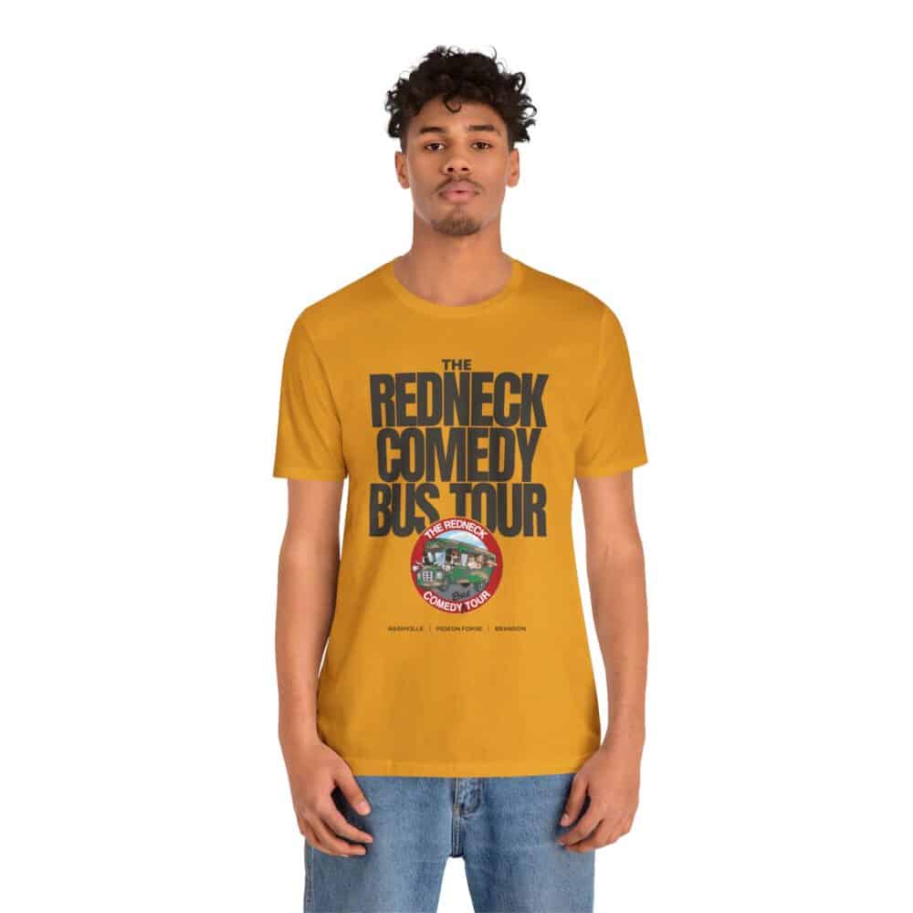 A man stands facing forward wearing the Redneck Comedy Bus Tour Tshirt, which is mustard yellow and features "The Redneck Comedy Bus Tour" and a circular tour bus logo on the front.