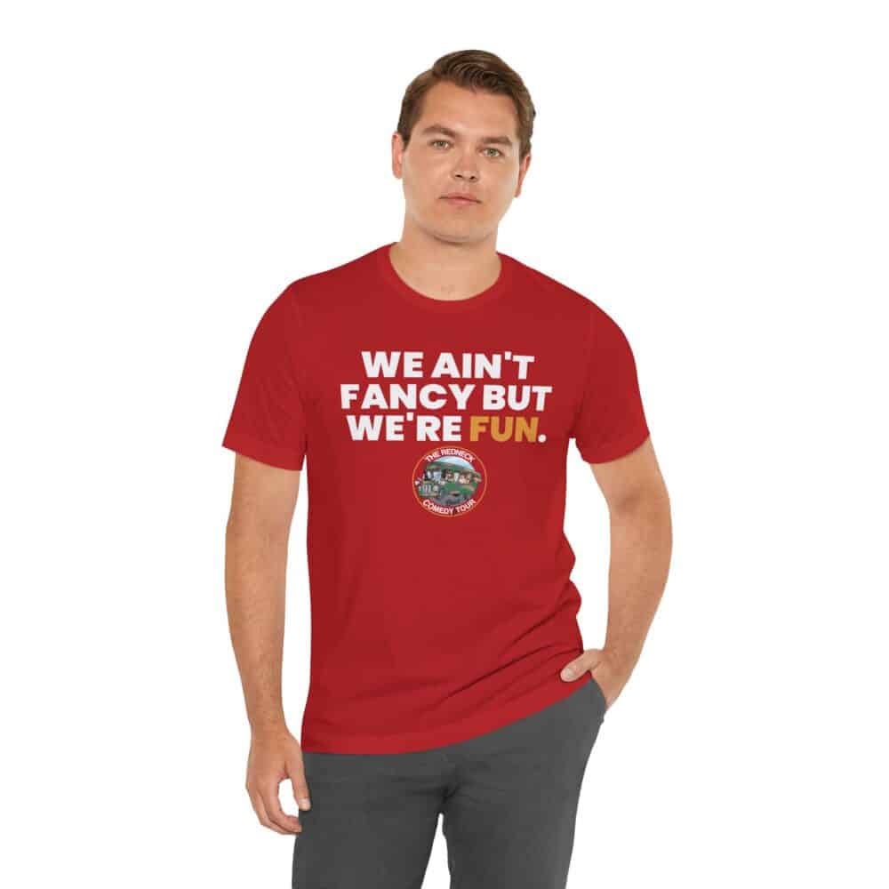 A man wears the "We Ain't Fancy Tshirt," a red shirt with white text reading "WE AIN'T FANCY BUT WE'RE FUN." and a small circular graphic below.
