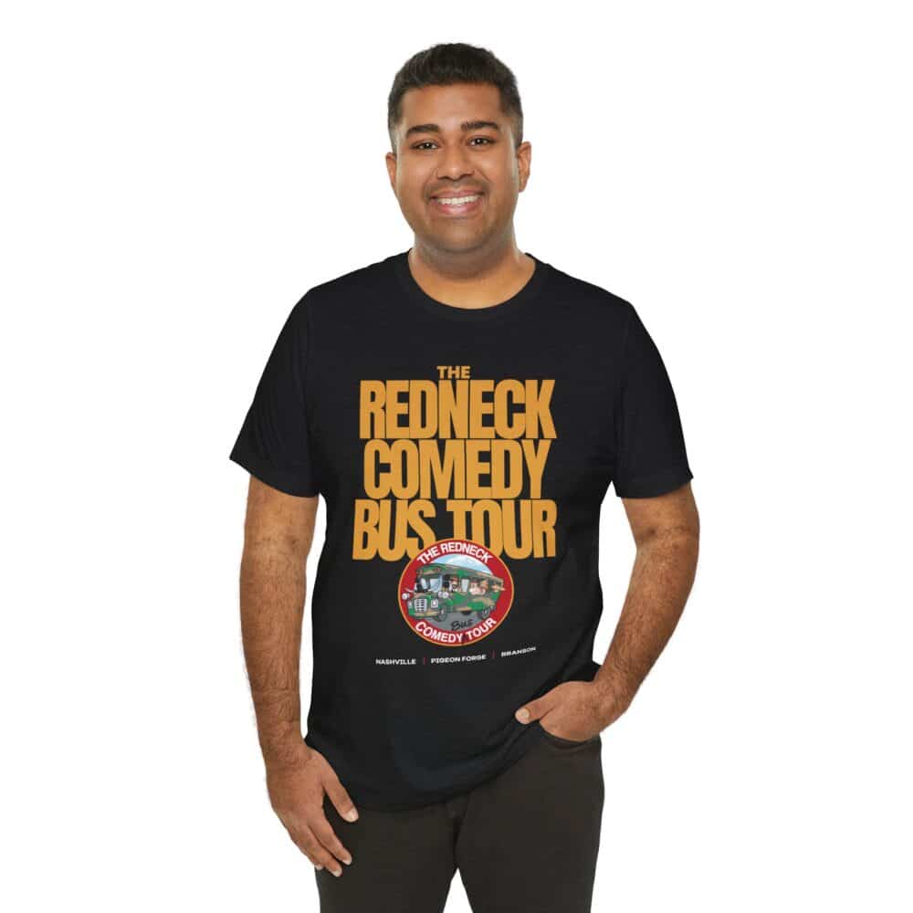 A man smiles at the camera, wearing the Redneck Comedy Bus Tour Tshirt featuring the tour name with a logo and bus graphic printed below.