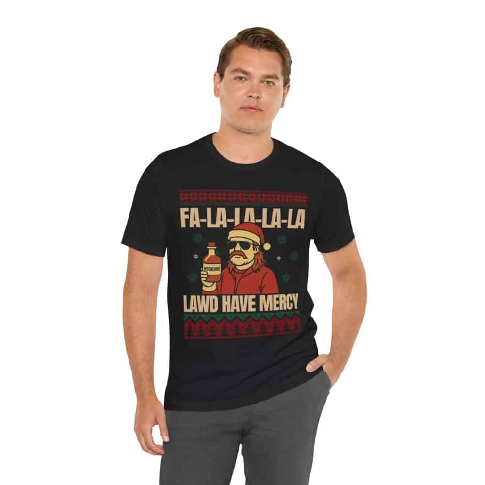 A man wearing the Christmas Ugly Sweater Redneck Tshirt with a festive graphic of a person holding a drink, Christmas-themed images, and the text "FA-LA-LA-LA-LA" and "LAWD HAVE MERCY.